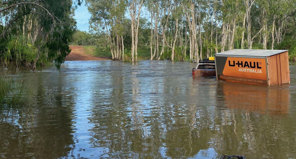 A ute with orange uHaul trailer stuck in floodwaters in the Blyth River, NT