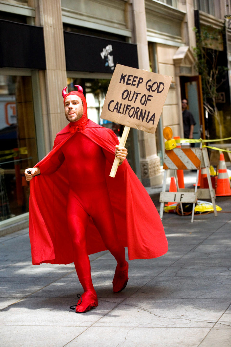 Chris, dressed as a devil and holding a protest sign that reads "Keep God Out of California"