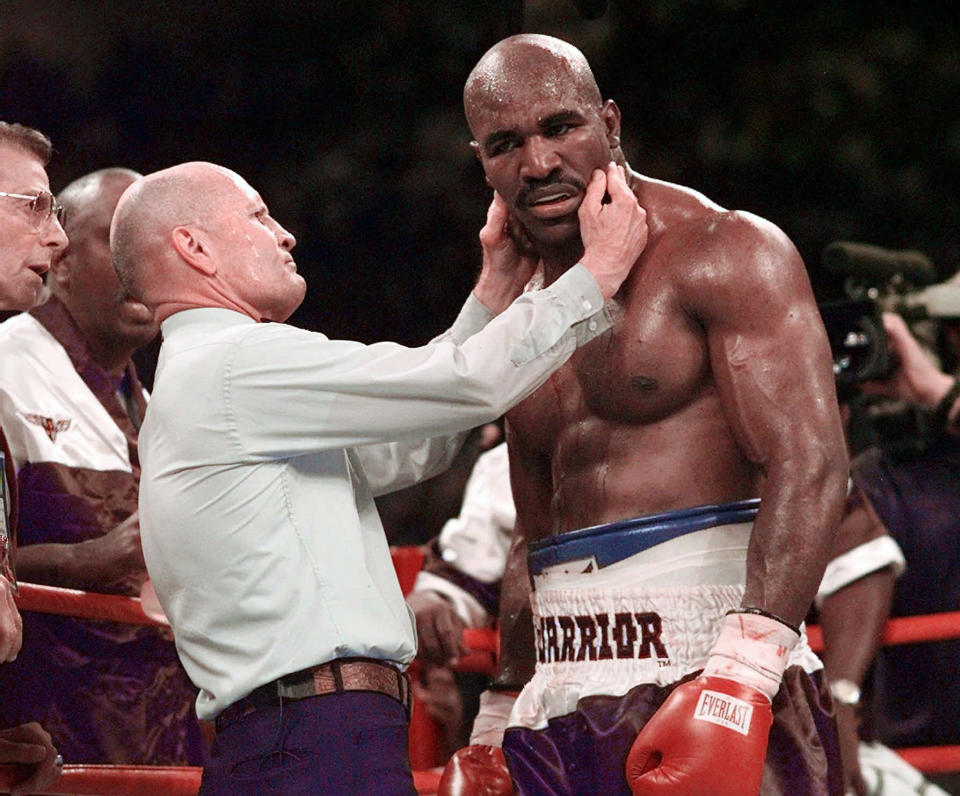 FILE - Evander Holyfield has his right ear checked by referee Mills Lane after he was bit on the ear by Mike Tyson during the third round of their WBA heavyweight boxing match June 28, 1997, in Las Vegas. Lane, the Hall of Fame boxing referee who was the third man in the ring when Tyson bit Holyfield’s ear, died Tuesday, Dec. 6, 2022. He was 85. Lane had suffered a stroke in 2002 and son Tommy said his father had taken a significant turn for the worse recently before entering hospice care Friday. (AP Photo/Mark J. Terrill, File)