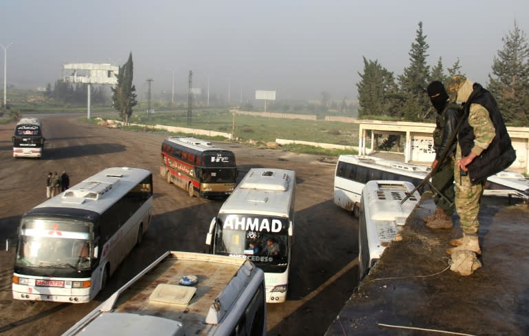 Syrian opposition fighters stand on top of a vehicle in rebel-held Rashidin, as buses evacuating people from government-held Fuaa and Kafraya arrive as part of an evacuation deal, on April 14, 2017