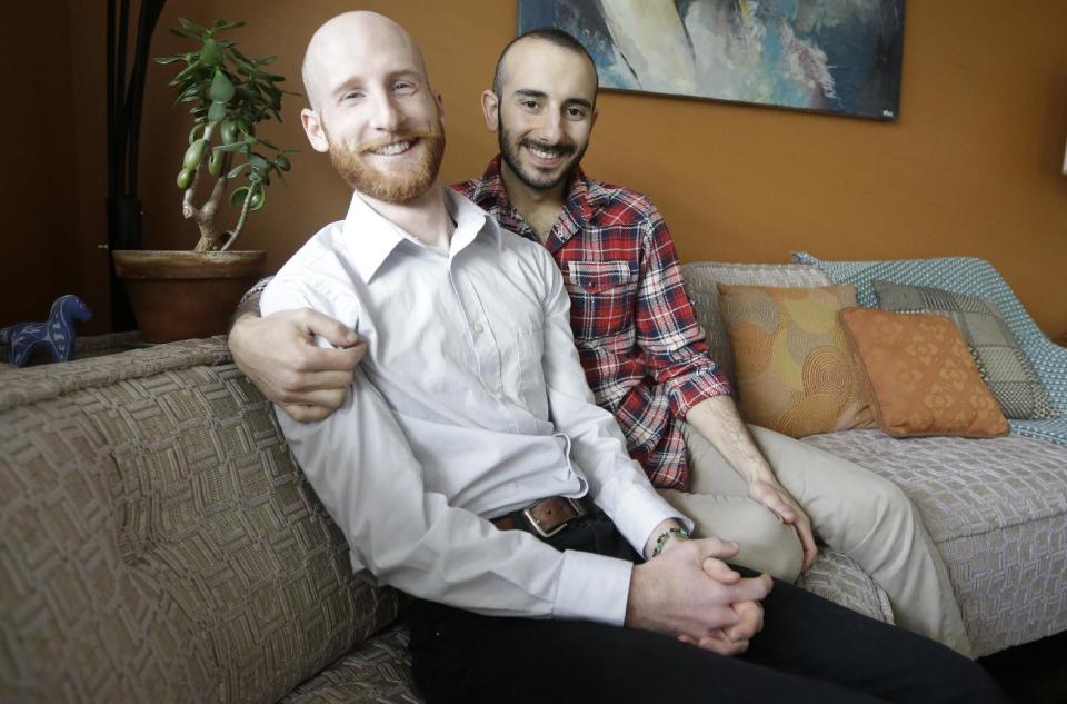 In this April 3, 2014, photo, Derek Kitchen, left, and Moudi Sbeity sit on their couch at their home, in Salt Lake City. The young couple that has become the face of gay marriage in Utah is an unlikely pair for the role. Kitchen and Sbeity were both raised in conservative religious families that shun gays, Kitchen in a Mormon home in Utah and Sbeity in a Muslim family in Lebanon. They each came out when they were 16 years old, worlds apart, and met six years later in college in Utah. They chose to become one of three couples as plaintiffs in the lawsuit challenging Utah’s same-sex marriage to publicly push back against religions that oppress gays and lesbians. (AP Photo/Rick Bowmer)