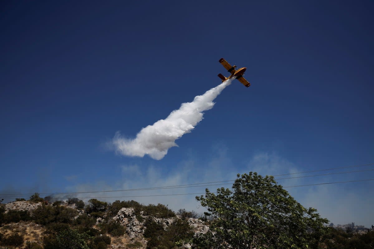 A plane drops water as firefighters try to extinguish a wildfire near the town of Koropi, close to Athens (REUTERS)