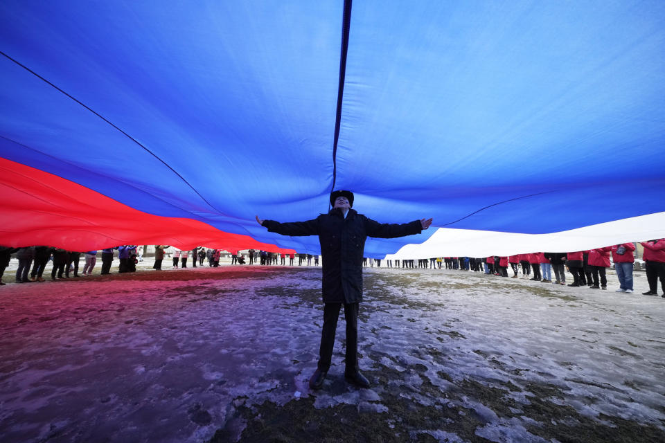 A Navy school cadet stands under a giant Russian flag during an action to mark the ninth anniversary of the Crimea annexation from Ukraine, in St. Petersburg, Russia, Saturday, March 18, 2023. (AP Photo/Dmitri Lovetsky)