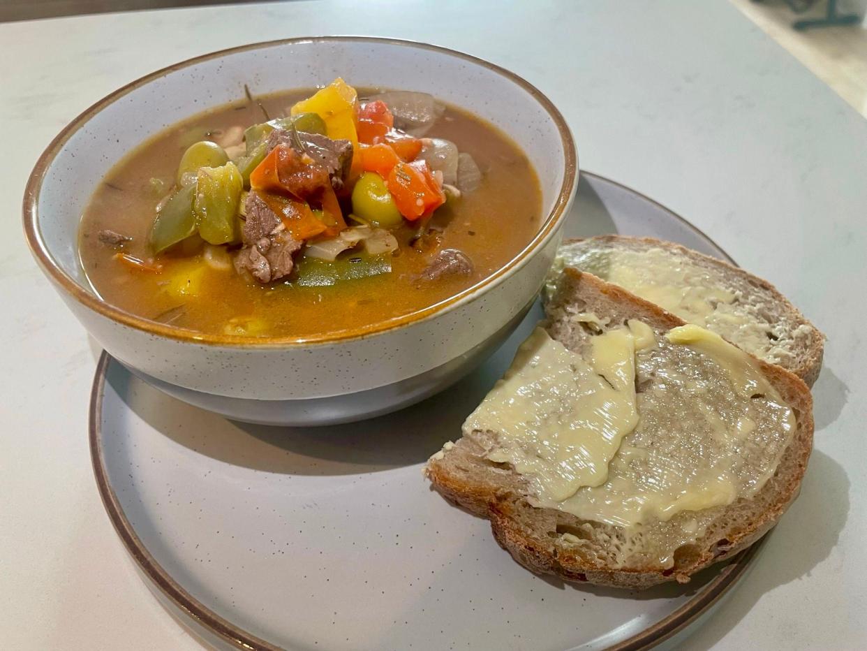 Beef stew in bowl with bread and butter on the side.