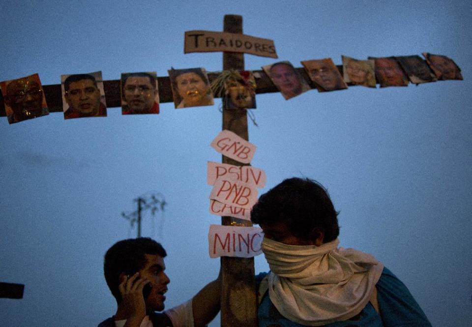 Manifestantes antigubernamentales portan una cruz cubierta con fotos de funcionarios del gobierno y seguidores del régimen bajo un letrero que dice "Traidores" durante un acto vinculado a la Semana Santa en Caracas, Venezuela, el miércoles 16 de abril de 2014. T(AP Photo/Ramon Espinosa)