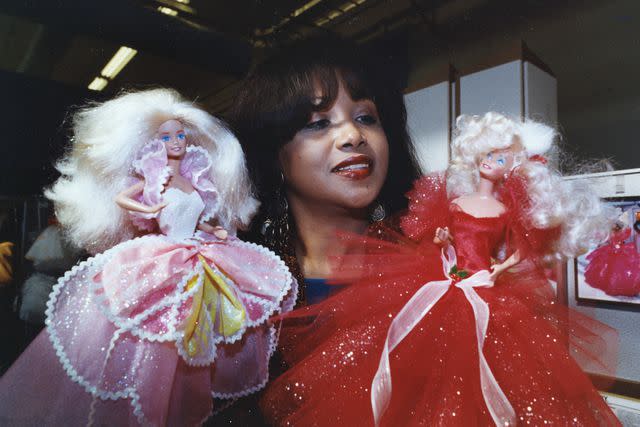 <p>LARRY BESSEL / LOS ANGELES TIMES / Getty</p> Kitty Black Perkins shows off two of her glittering creations for Barbie dolls at the Mattel offices in El Segundo, CA. on January 29, 1991.