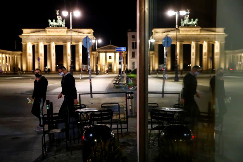 People wearing face masks walk by an empty table of a cafe in front of the Brandenburg Gate, in Berlin