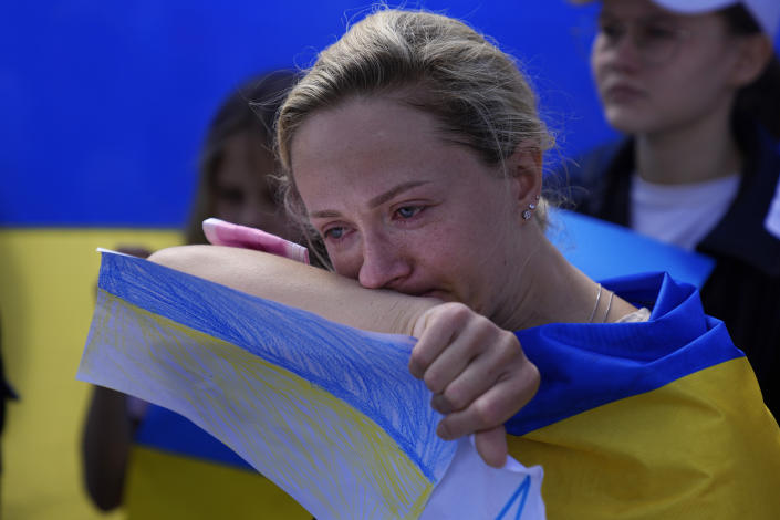 A woman tears up as she holds a roughly colored paper in the colors of the Ukrainian flag.