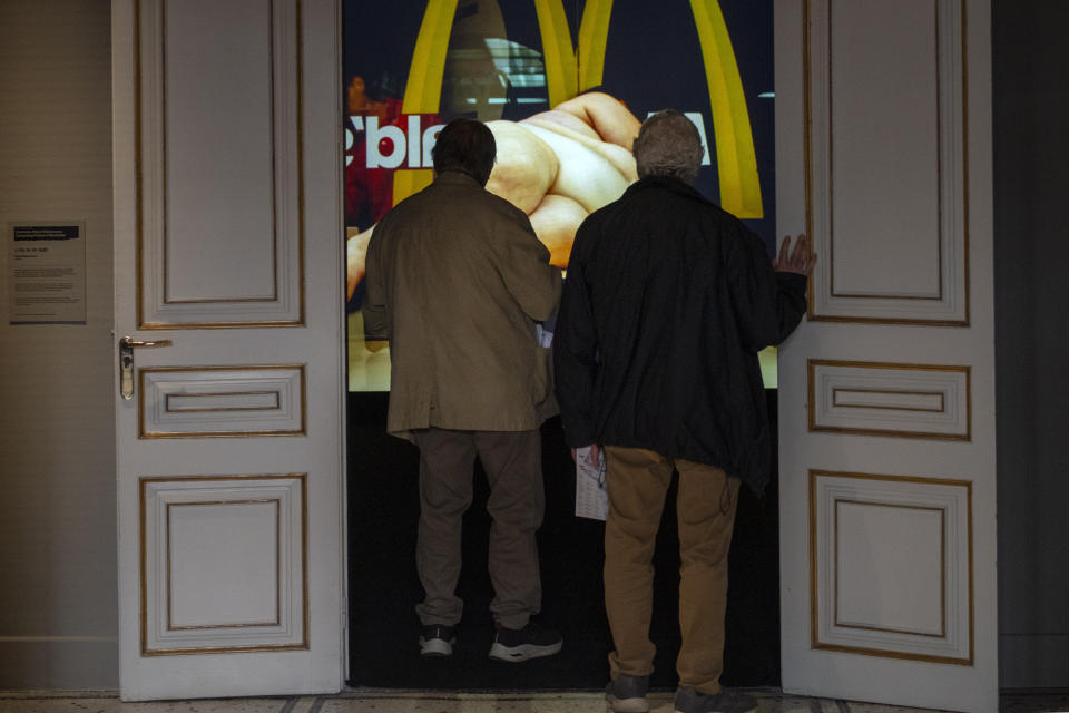 Visitors look at Yoshua Okón's video of an obese woman lying nude on a table in McDonald's, called "Freedom Fries," at Barcelona's Museum of Forbidden Art in Barcelona, Spain, Wednesday, Nov. 8, 2023. Yoshua Okón's video was removed from a gallery in London after, according to the Barcelona museum, members of gallery's board were worried about damaging the fast-food chain's reputation. A new museum in Barcelona is offering a second chance to controversial artworks that have suffered censorship for religious, sexual, political or commercial reasons. (AP Photo/Emilio Morenatti)