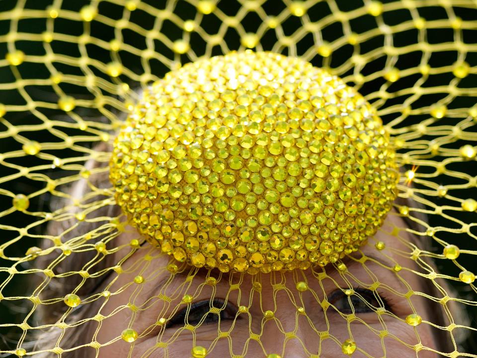 A close-up of a person wearing a yellow bedazzled hat with a mesh and glitter detail at the Royal Ascot racing event.