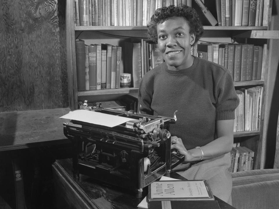 Black and white photo of Gwendolyn Brooks smiling and writing on a typewriter