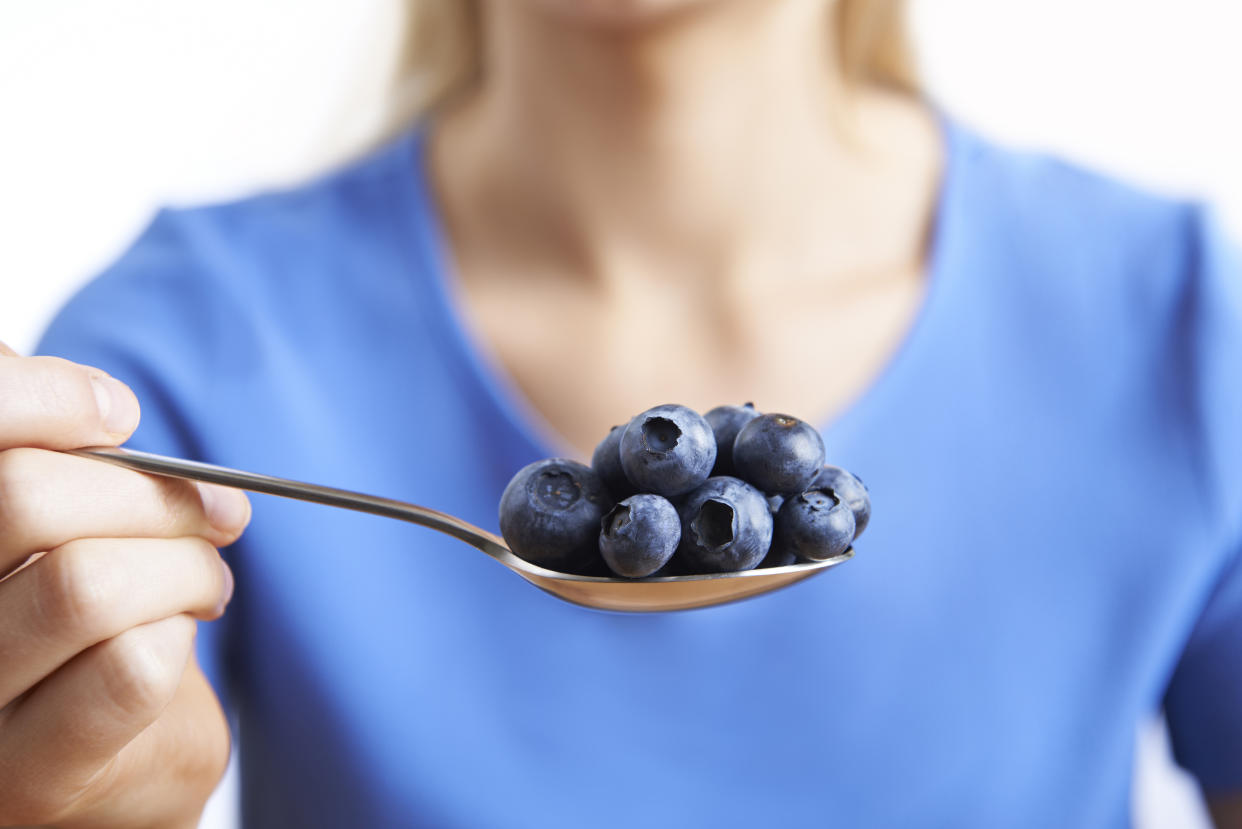 A woman holding a spoon filled with blueberries.