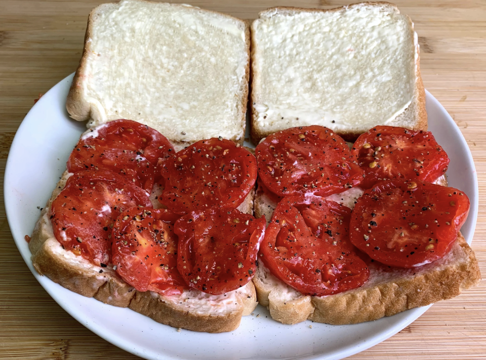 An open-faced sandwich with sliced tomatoes, mayonnaise, and pepper on white bread, placed on a white plate