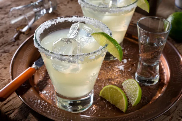 A margarita on the rocks with a salted rim, garnished with a lime wedge