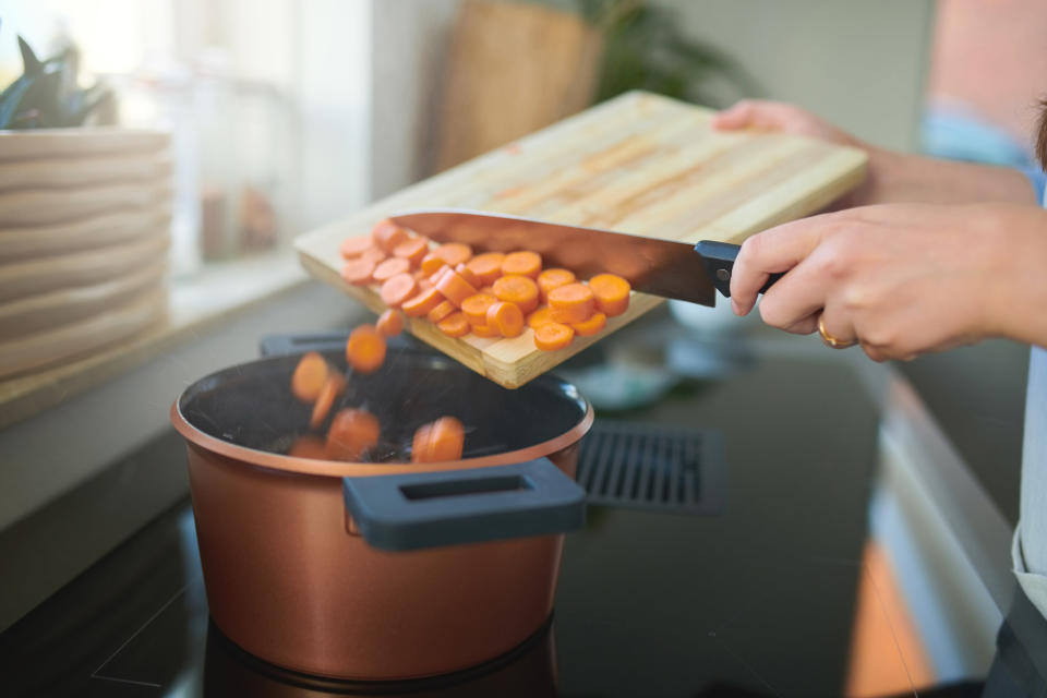 Adding carrots to a pot of stew on the stovetop.