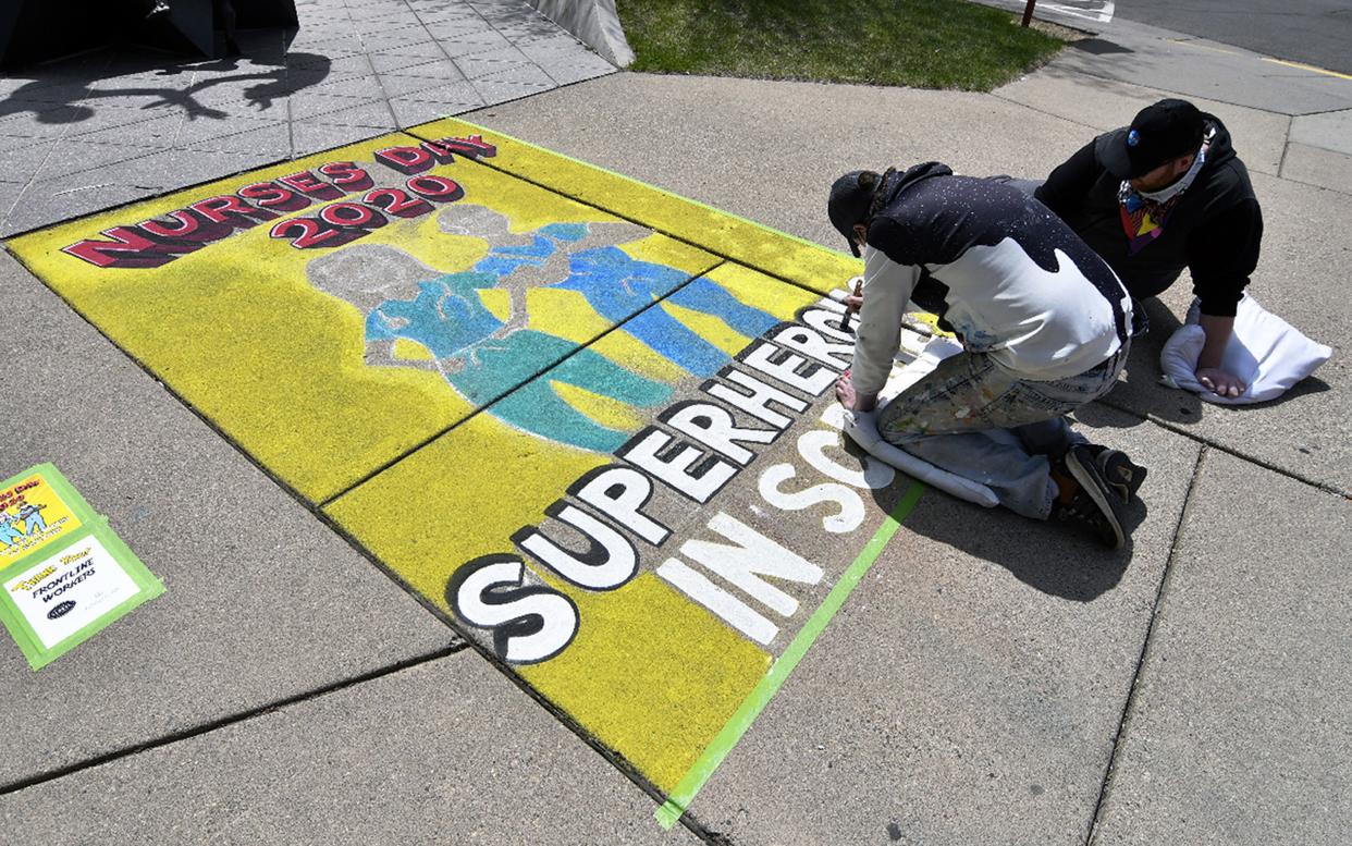 Local artist Shane Anderson, left, and Matt Hintz create a chalk art tribute near the entrance to Abbott Northwestern Hospital with a custom "thank you" design on the sidewalk near the entrance of the hospital entitled, "Superheroes in Scrubs," on Wednesday, May 6, 2020, in Minneapolis, Minnesota. The day was National Nurses Day.