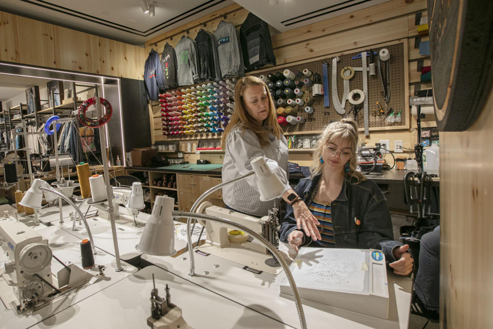 In this June 14, 2019, photo Sue Ceccarelli, left, Vice President of Retail Operations for Levi Strauss & Co.. talks with with tailor Aly Reinert in the Levi's Tailor Shop, in the Levi's store, in New York's Times Square. Levi Strauss & Co.’s new flagship in Manhattan’s Time Square features larger dressing rooms with call buttons and tailors who can add trims and patches to customers’ jeans. (AP Photo/Richard Drew)