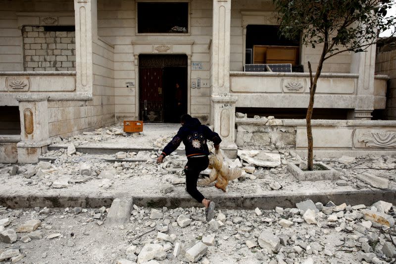 A Syrian boy removes a dead chicken from the debris of a building hit by an air strike in Idlib