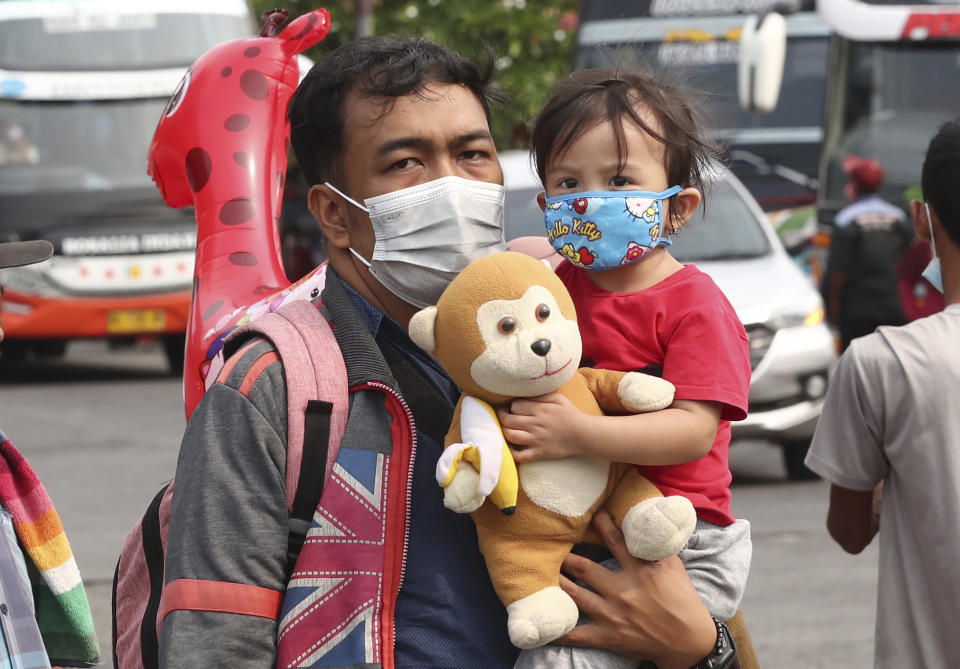 A man carries his daughter at the Kalideres bus terminal in Jakarta, Indonesia, Wednesday, May 5, 2021. The mass exodus out of major cities in the world's most populous Muslim country is underway despite travel restrictions imposed by the government to prevent the spread of coronavirus outbreak, as people are heading home to their villages to celebrate Eid al-Fitr holiday that marks the end of the holy fasting month of Ramadan on May 13. (AP Photo/Tatan Syuflana)