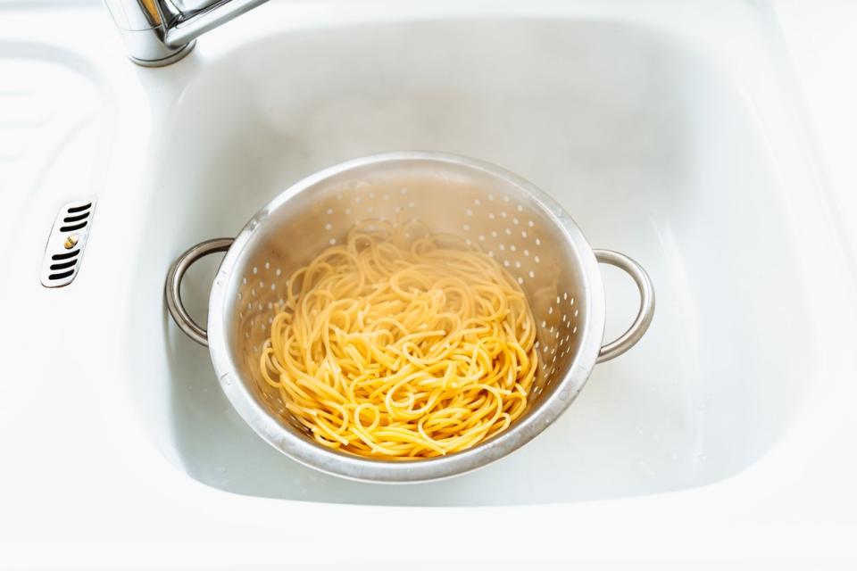 Boild spaghetti in a white colander, inside a white kitchen sink. 