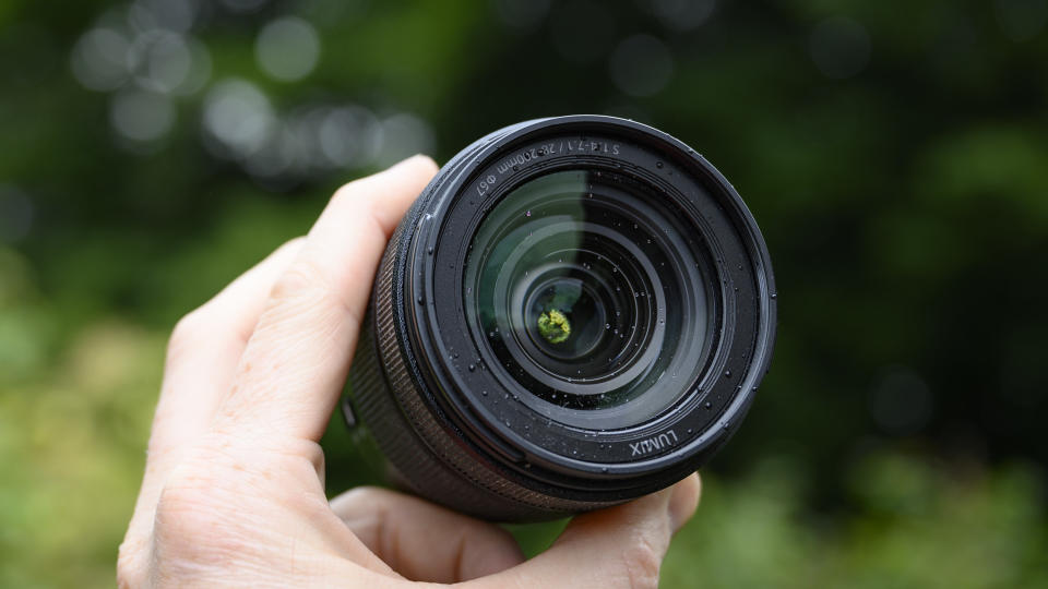 Panasonic Lumix S 28-200mm travel lens in the hand with leafy background and light rain