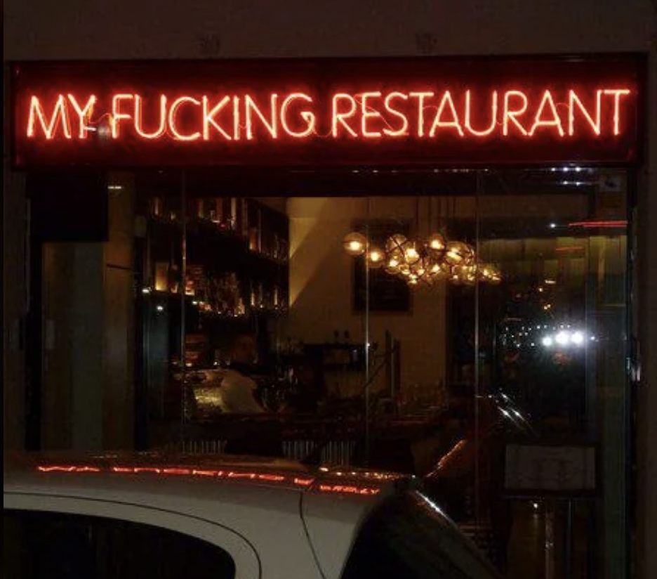 Semn neon pentru un restaurant cu nume provocator deasupra ferestrei sale