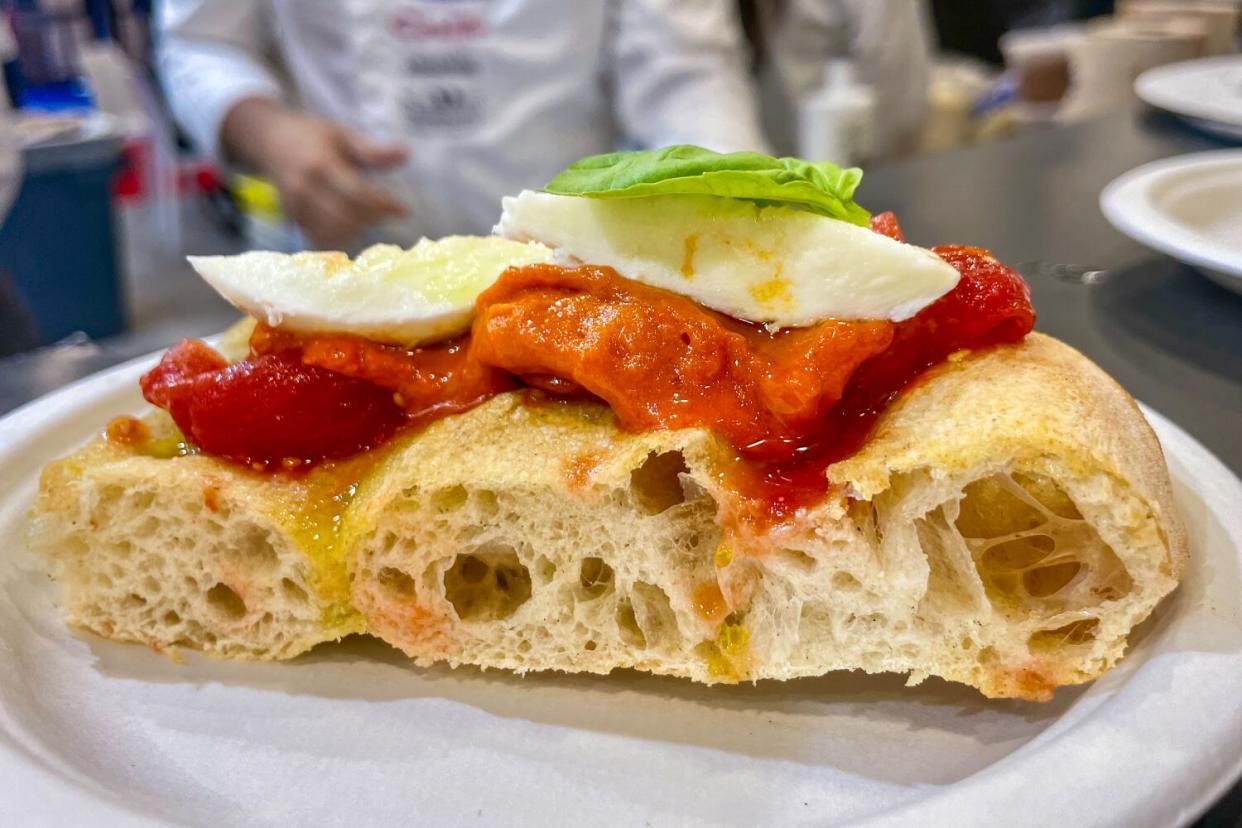A slice of spianata focaccia topped with crushed tomato, mozarella di bufala and fresh basil