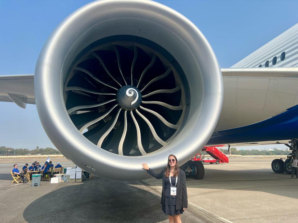 The author in a black blazer and black dress standing next to the giant GE9X engine in India.