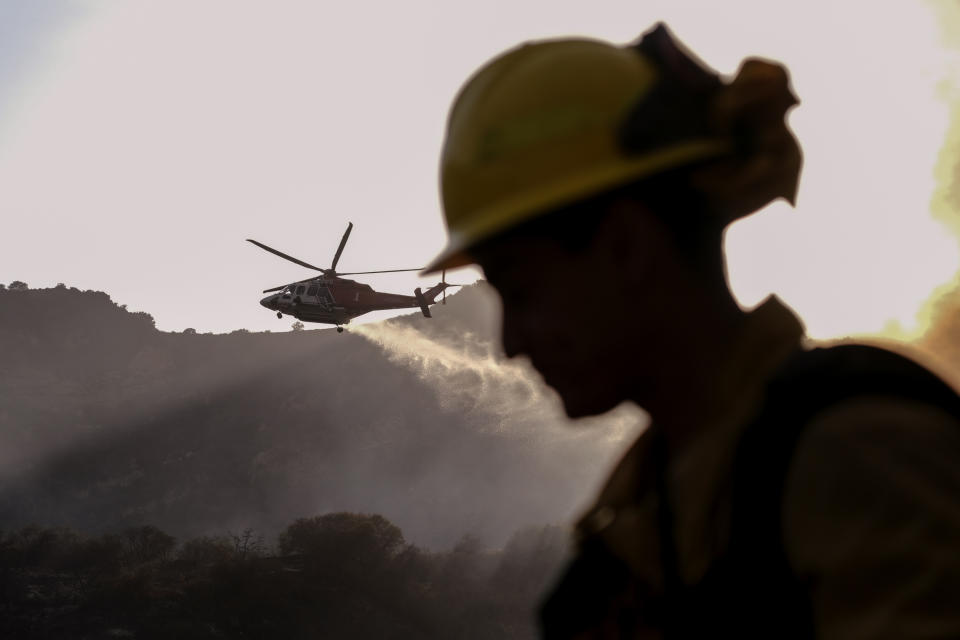 A firefighter keeps watch as a firefighting helicopter drops water on a brush fire scorching at least 100 acres in the Pacific Palisades area of Los Angeles on Saturday, May 15, 2021. (AP Photo/Ringo H.W. Chiu)