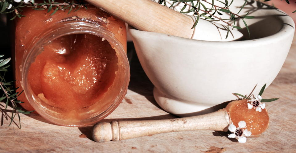 A background of manuka honey in a wooden spoon with a manuka flowers.