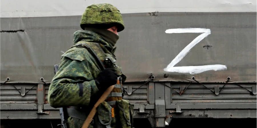 A Russian soldier stands next to a military truck marked with a 