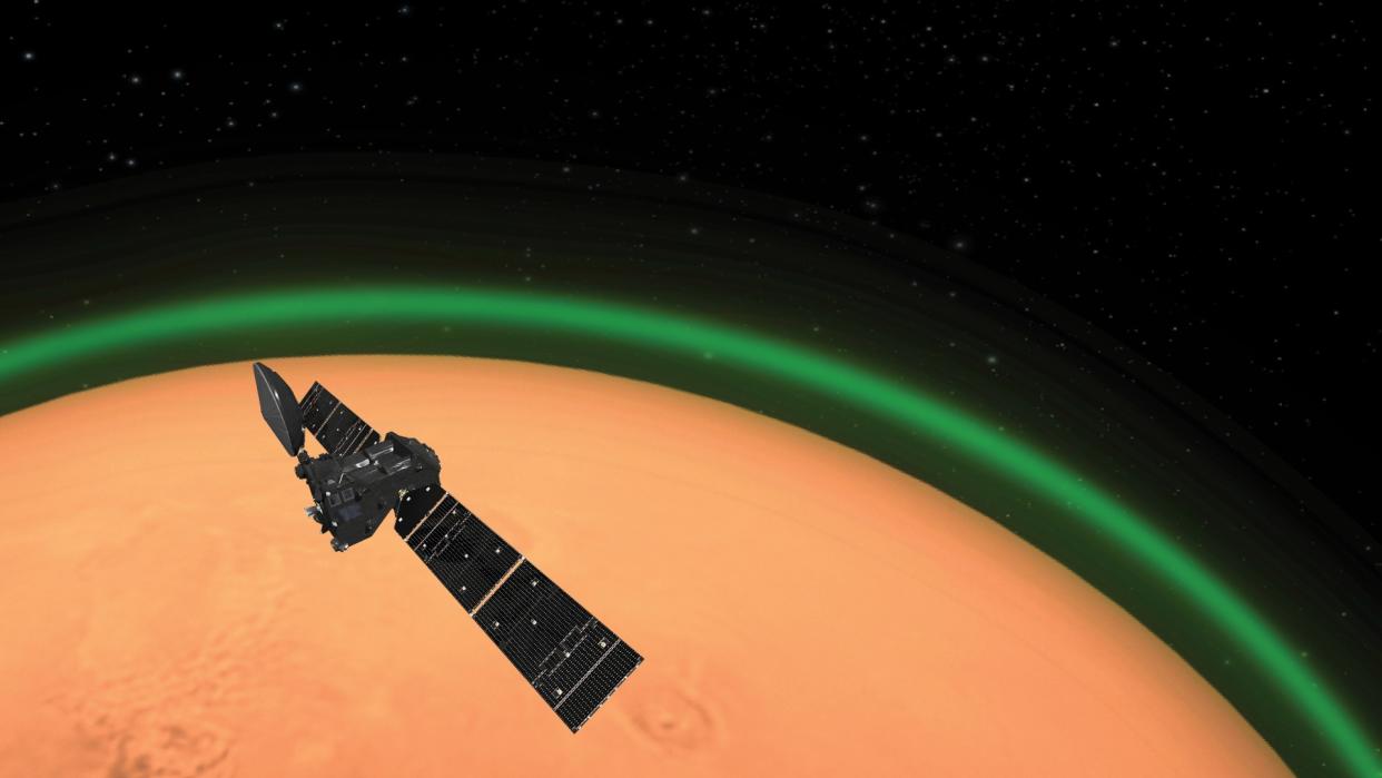  A greenish glow can be seen behind a spacecraft with two large solar panels above Mars. 