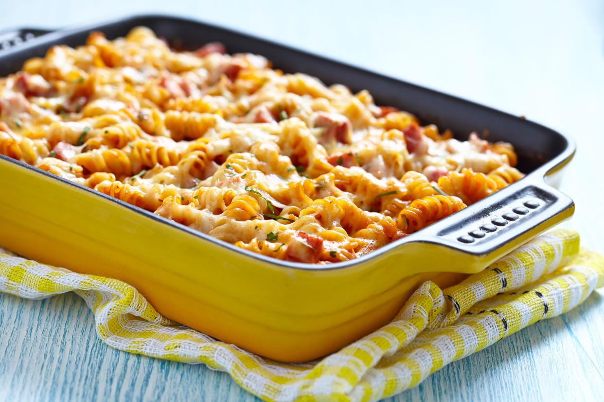 Closeup of cheesy chicken and spinach pasta bake on a yellow rectangle ceramic cooking pot on a yellow napkin on a blue wooden table