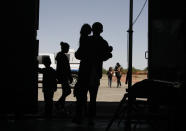 CORRECTS DAY - In this Wednesday, May 22, 2019, migrants mainly from Central America guide their children through the entrance of a World War II-era bomber hanger in Deming, N.M. A surge of asylum-seeking families has been straining cities along the southern U.S. border for months, but now the issue is flowing into cities far from Mexico, where immigrants are being housed in an airplane hangar and rodeo fairgrounds and local authorities are struggling to keep up with the influx. (AP Photo/Cedar Attanasio)