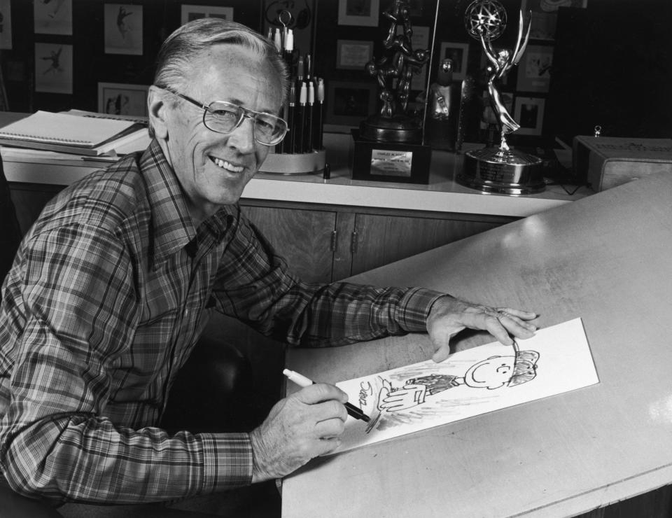 1978:  Portrait of American cartoonist Charles M Schulz (1922 - 2001), creator of the 'Peanuts' comic strip, sitting at his studio drawing table with a picture of his character Charlie Brown and some awards behind him. Schulz created the comic strip in 1950.  (Photo by CBS Photo Archive/Getty Images)