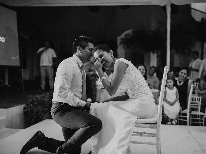 a black and white photo of a groom getting ready to take off his laughing bride's garter