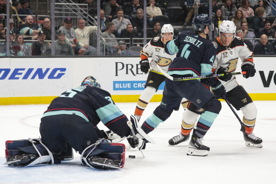 Seattle Kraken goaltender Joey Daccord (35) covers the puck and defenseman Justin Schultz (4) defends as Anaheim Ducks center Ryan Strome (16) moves in during the second period of an NHL hockey game Tuesday, March 26, 2024, in Seattle. (AP Photo/Jason Redmond)