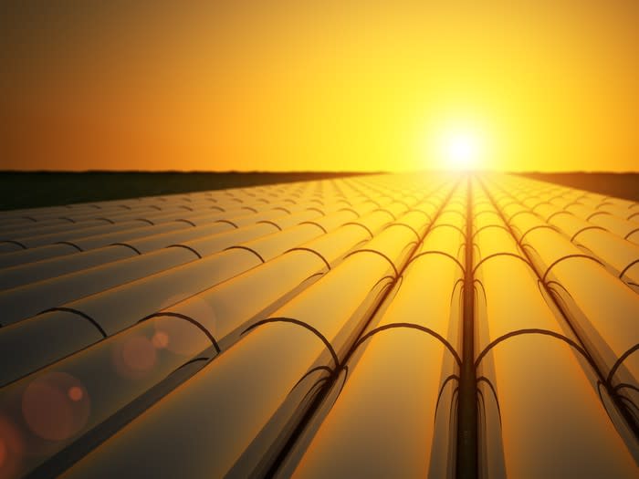 Rows of oil pipeline with the sun setting over them in the distance.