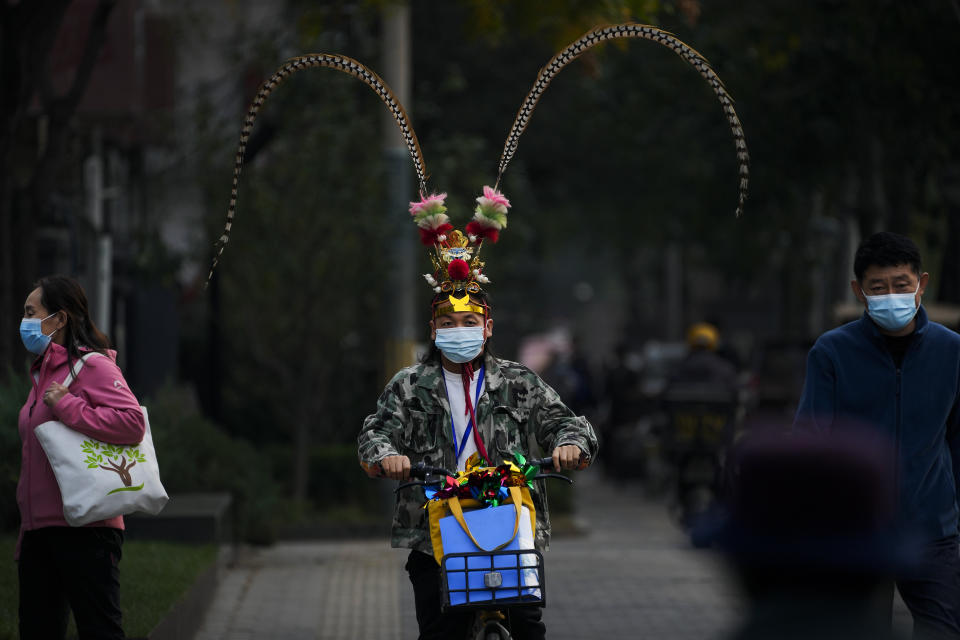 A man wearing a face mask dressed with Monkey King costume headgear rides past masked residents on a street in Beijing, Wednesday, Nov. 2, 2022. (AP Photo/Andy Wong)