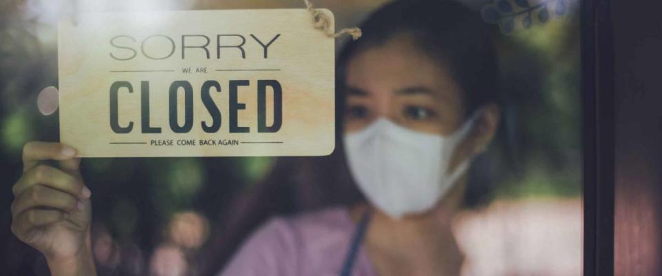 Close up shot of woman wearing mask and hand turning closed sign board on glass door in coffee shop and restaurant after coronavirus lockdown quarantine.Business crisis concept.