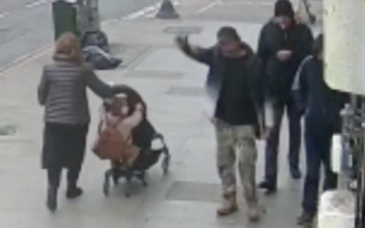 Image of man raising his arm as he walks past woman and two children on the street