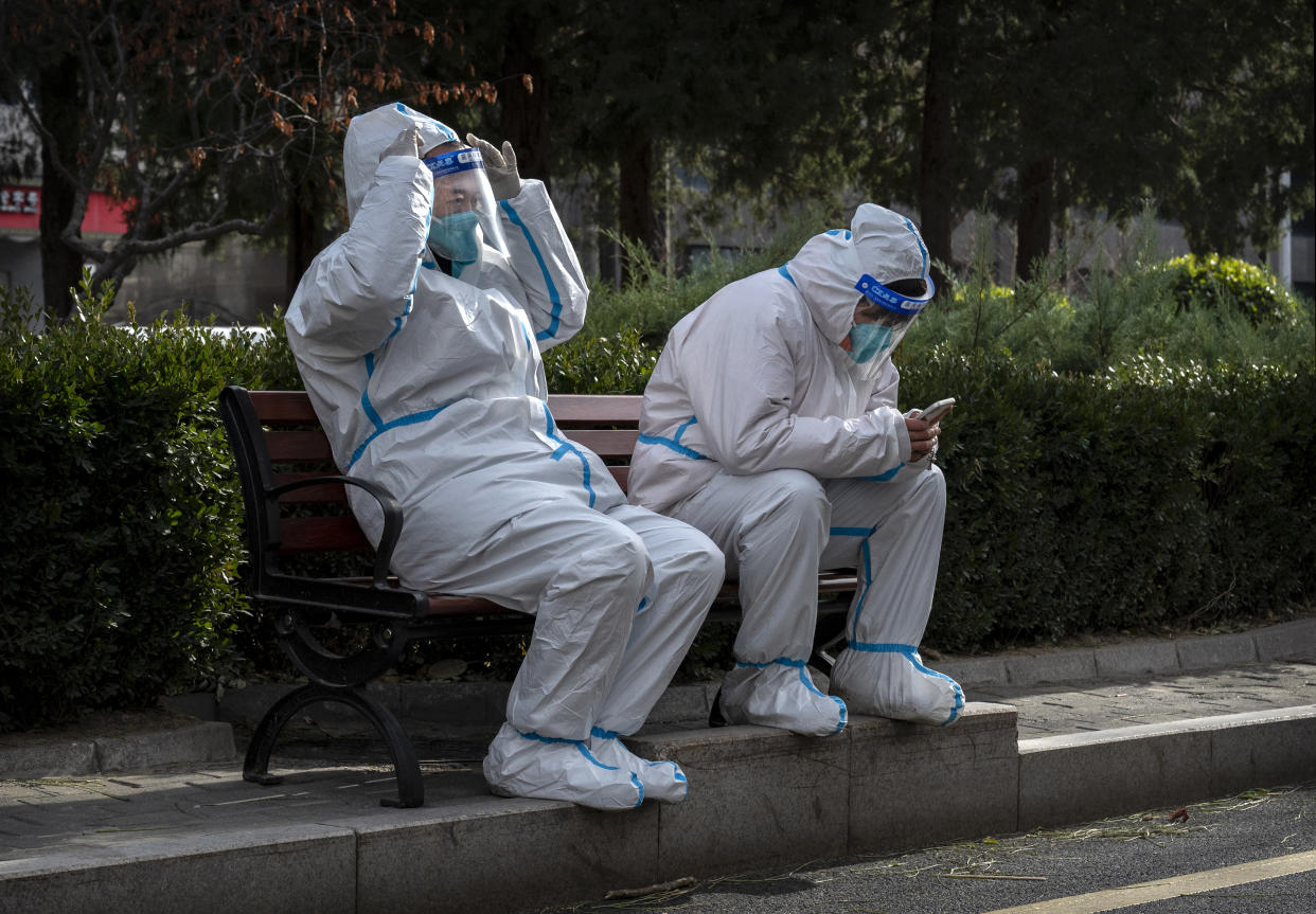 BEIJING, CHINA - NOVEMBER 29: Epidemic control workers wear PPE to prevent the spread of COVID-19 as they rest on a park bench in an area where communities are in lockdown on November 29, 2022 in Beijing, China. In recent days, China has been recording its highest number of daily COVID-19 cases since the pandemic began, as authorities are sticking to their strict zero tolerance approach to containing the virus with lockdowns, mandatory testing, mask mandates, and quarantines as it struggles to contain outbreaks.In an effort to try to bring rising cases under control, the government last week closed most stores and restaurants for inside dining, switched  schools to online studies, and told people to work from home among other measures. (Photo by Kevin Frayer/Getty Images)