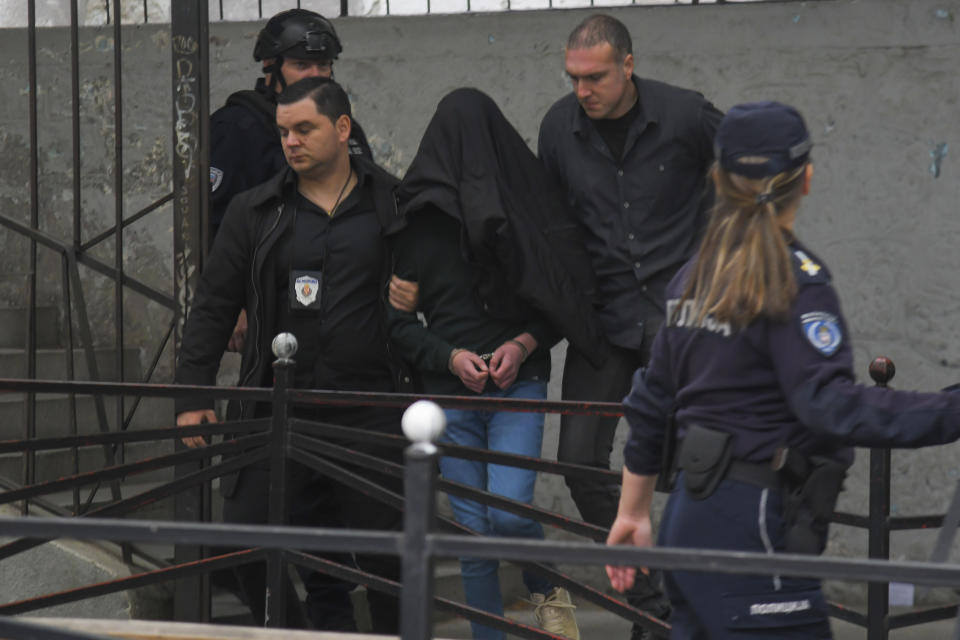 A suspect is escorted by police outside the Vladislav Ribnikar school in Belgrade, Serbia, Wednesday, May 3, 2023. Serbian police say a teenage boy opened fire at a school in central Belgrade, killing several people and injuring several more. (AP Photo)