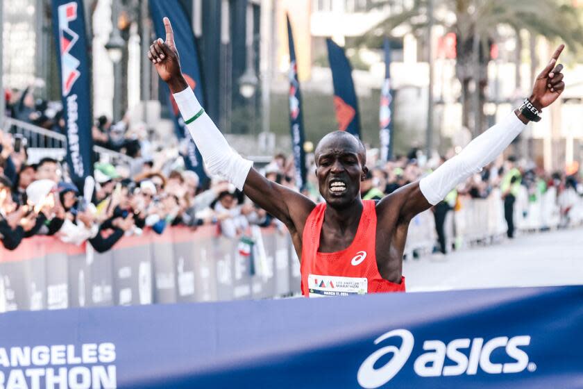 Dominic Ngeno raises his arms as he crosses the finish line, winning the elite male division of the 39th L.A. Marathon