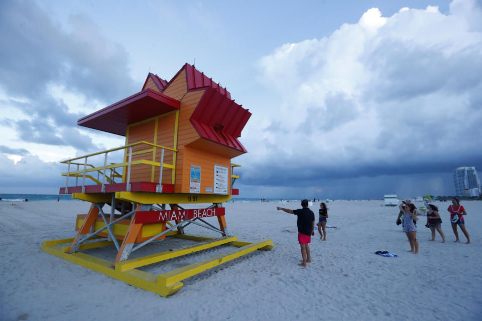 Beach goers on South Beach check out one of the iconic lifeguard stands as bands of rain fall in the distance, Friday, Aug. 30, 2019, on Miami Beach, Fla. All of Florida is under a state of emergency and authorities are urging residents to stockpile a week&#39;s worth of food and supplies as Hurricane Dorian gathers strength and aims to slam the state as soon as Monday as a Category 4 storm. (AP Photo/Wilfredo Lee)