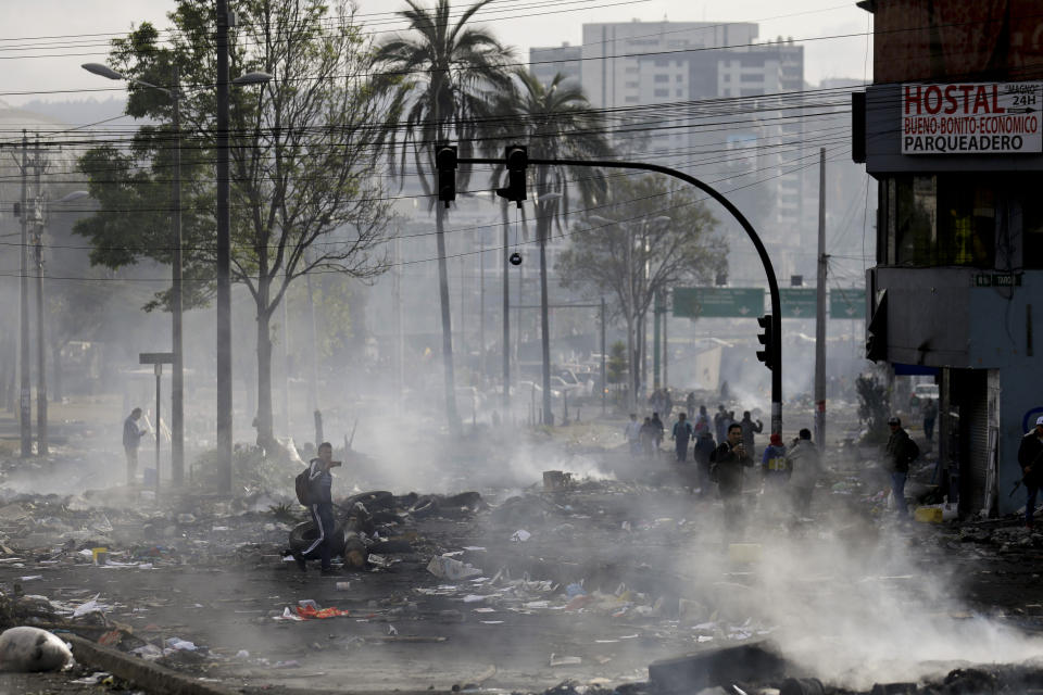 Pedestrians walk among the debris of barricades set by anti-government protesters in Quito, Ecuador, Sunday, Oct. 13, 2019. President Lenin Moreno ordered the army onto the streets of Ecuador's capital Saturday after a week and a half of protests over fuel prices devolved into violent incidents. (AP Photo/Fernando Vergara)