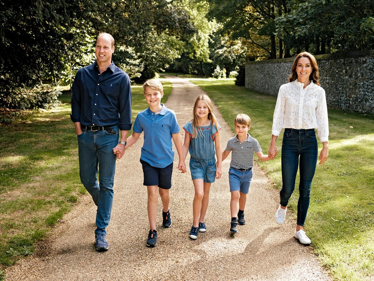 Prince William, Prince George, Princess Charlotte, Prince Louis, and Kate Middleton hold hands and smile as they walk down a path.