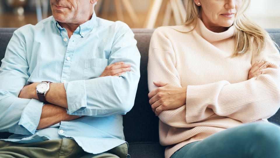 mature couple sitting on the sofa with their arms folded after an argument.