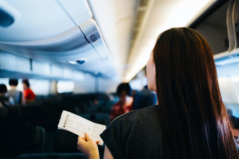 A stock image of a person on a plane holding their boarding pass.