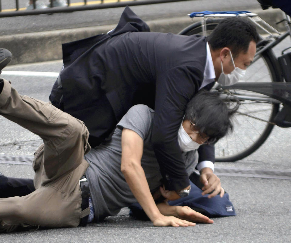 FILE - Tetsuya Yamagami, bottom, is detained near the site of gunshots in Nara Prefecture, western Japan, Friday, July 8, 2022. Yamagami allegedly killed former Japanese Prime Minister Shinzo Abe during a campaign speech in Nara. A glimpse of his painful childhood has led to a surprising amount of sympathy in Japan, where three decades of economic malaise and social disparity have left many feeling isolated and unease. (Katsuhiko Hirano/The Yomiuri Shimbun via AP, File)